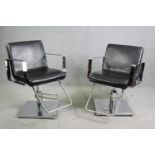 A pair of adjustable chrome barber's chairs in faux leather upholstery.