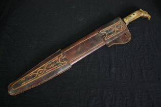 A sword with engraved blade in stitched leather scabbard, possibly a central American saddle