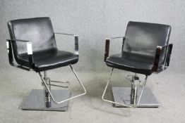 A pair of adjustable chrome barber's chairs in faux leather upholstery.