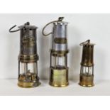 Three miner's lamps, including a Thomas and Williams, J H Naylor of Wigan, and another. Largest is