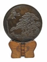An early 20th century Japanese bronze Kagami mirror on wooden stand, decorated with a pine tree