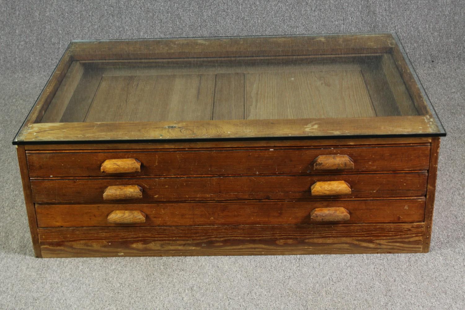 A 1920's pine planners chest, with later glass top to form a coffee table. H.40 W.123 D.92cm.