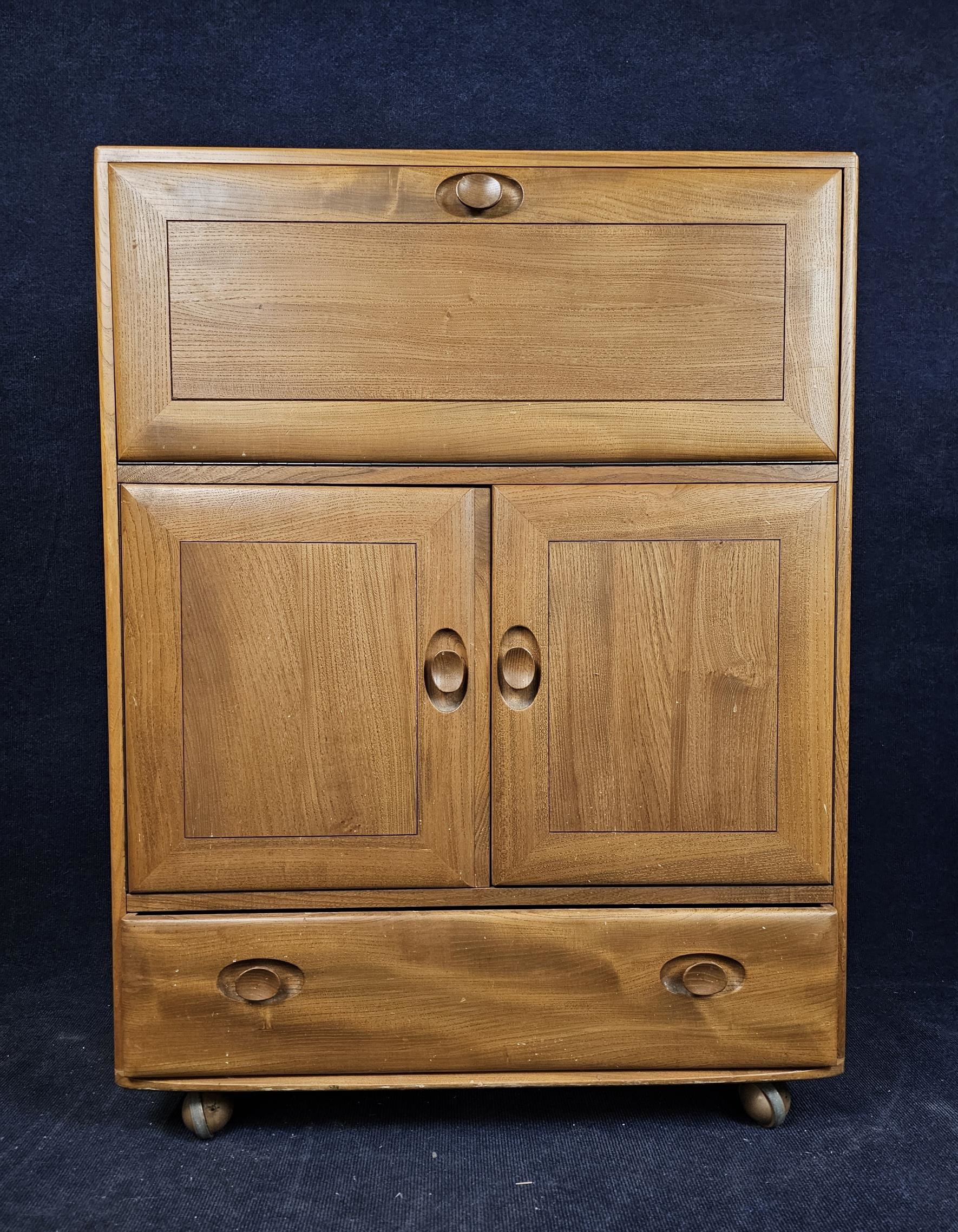 An Ercol elm side cabinet with fall front. H.110 W.83 D.45.cm