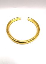 A yellow metal (tests as 22ct yellow gold) solid bangle with raised foliate design. Aperture