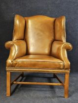 A George III style oak wingback armchair, with studded tan leather upholstery, 20th century, (