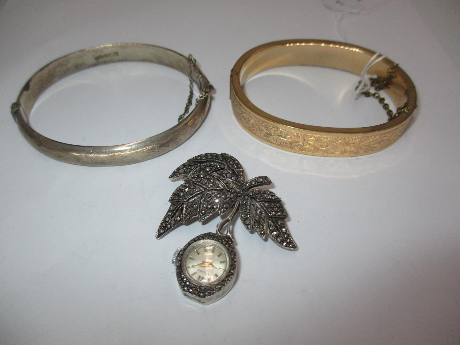 Silver and Marcasite Nivada Brooch Watch, a Silver Bangle and a Gold Plated Bangle