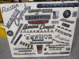 A COLLECTION OF VINTAGE CAR BADGES MOUNTED ON A WOODEN BOARD