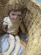 A VINTAGE ARMAND MARSEILLE CERAMIC HEADED DOLL CONTAINED IN A WICKER BASKET