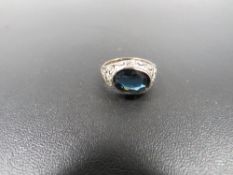 AN ORNATE DRESS RING SET WITH OVAL BLUE STONE ON LATER YELLOW METAL HALF BAND