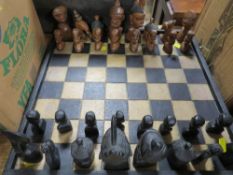 A CARVED WOODEN CHESS SET AND BOARD DEPICTING AFRICAN STYLISED PIECES