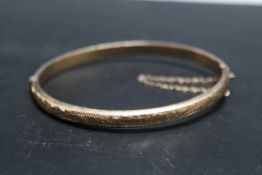 A HALLMARKED 9 CARAT GOLD HINGED BANGLE, with typical ornate engraving to front section, approx