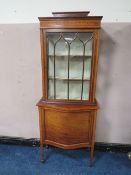 AN EDWARDIAN MAHOGANY INLAID DISPLAY CABINET, the serpentine fronted lower section with single door,