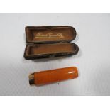 A CASED AMBER CHEROOT HOLDER WITH HALLMARKED 9 CARAT GOLD BAND