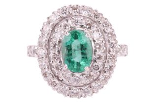 An emerald and diamond cluster ring, set with a central oval emerald measuring 7.6 x 5.4 x 3.6mm,