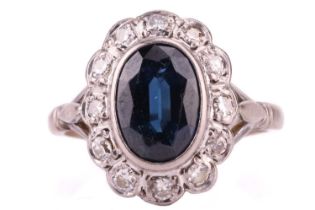 A sapphire and diamond entourage ring, centred with an oval-cut sapphire of dark greenish-blue