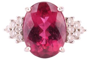 A rubellite and diamond ring, the oval rubellite centrally set in a four claw mount on a ribbed