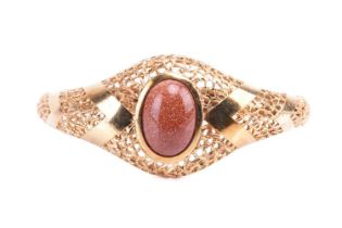 An oval hinged bangle, bezel set with a cabochon goldstone measuring approximately 16mm x 11mm, in a