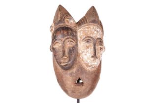A Baule ‘Janus’ two-faced portrait mask, mid-20th century, 30 cm high. NB: Display stand is for