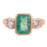 An emerald and diamond three stone ring, set with an emerald measuring 8 x 6 x 3.6mm, flanked by rou