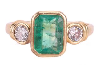 An emerald and diamond three stone ring, set with an emerald measuring 8 x 6 x 3.6mm, flanked by rou