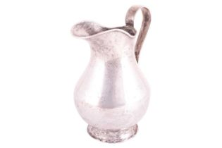 A white metal jug possibly Bolivian of baluster form with a tapered loop handle and flared foot,