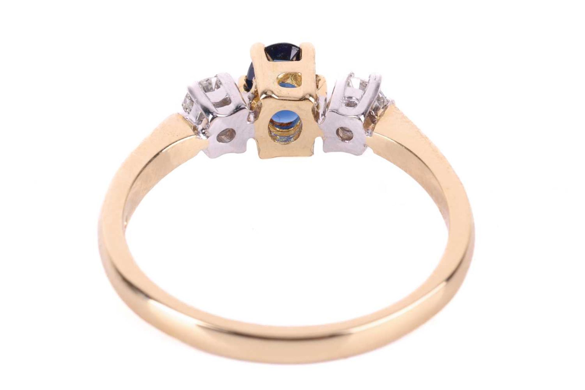 A sapphire and diamond trilogy ring in 18ct gold, centred with an oval-cut sapphire of dark blue col - Image 4 of 4