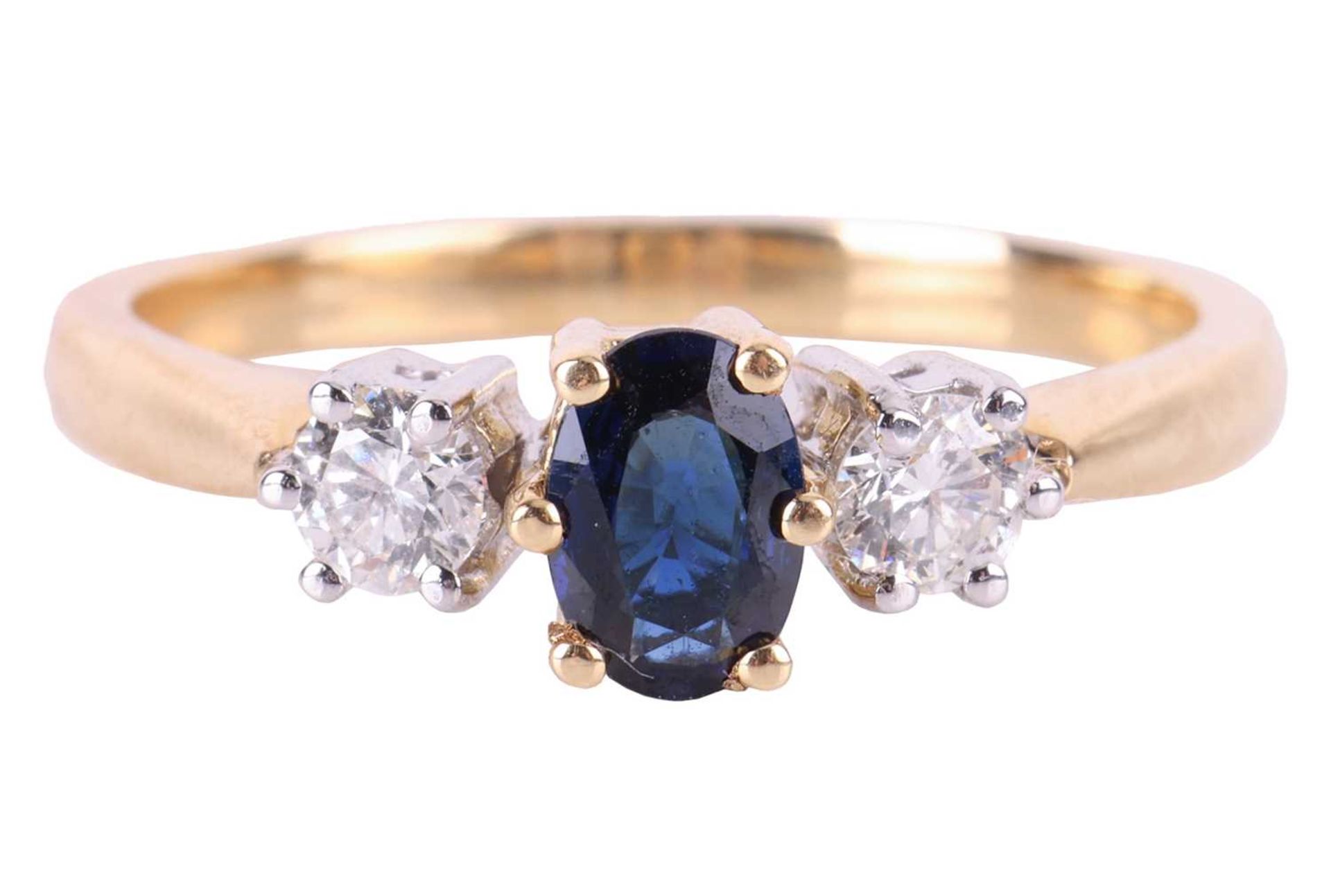 A sapphire and diamond trilogy ring in 18ct gold, centred with an oval-cut sapphire of dark blue col