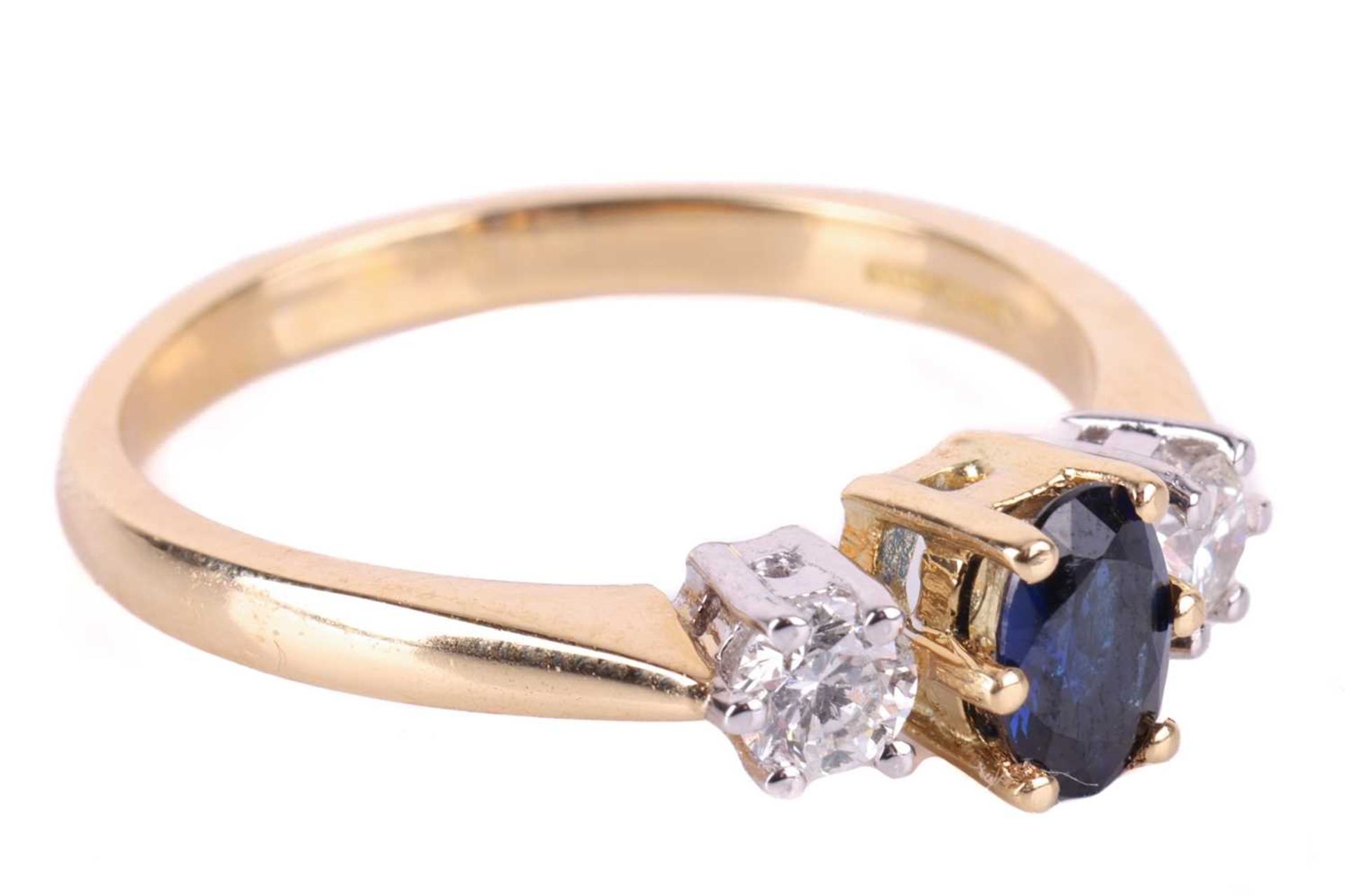 A sapphire and diamond trilogy ring in 18ct gold, centred with an oval-cut sapphire of dark blue col - Image 2 of 4