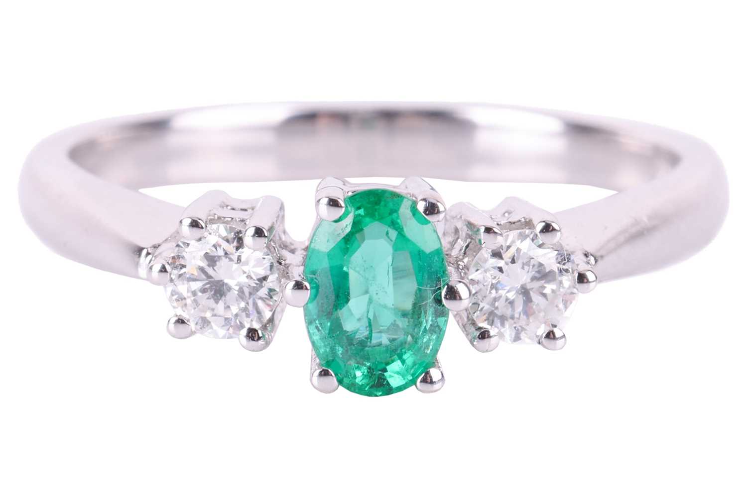 An emerald and diamond trilogy ring in 18ct white gold, centred with an oval-cut emerald of bright g