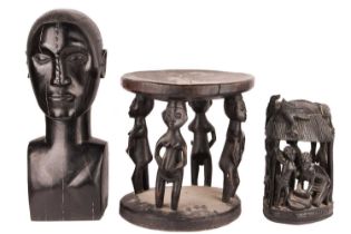 An African-carved wooden stool with figural supports on a circular base, alongside a large blackwood