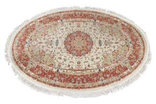 An oval ivory ground Tabriz rug with a central boss within a foliage border, 220 cm long x 150 cm