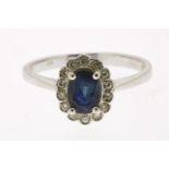 White gold entourage ring, centrally set with a blue colored stone in an entourage of diamonds,