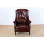 Brown leather armchair with black piping on wooden legs.