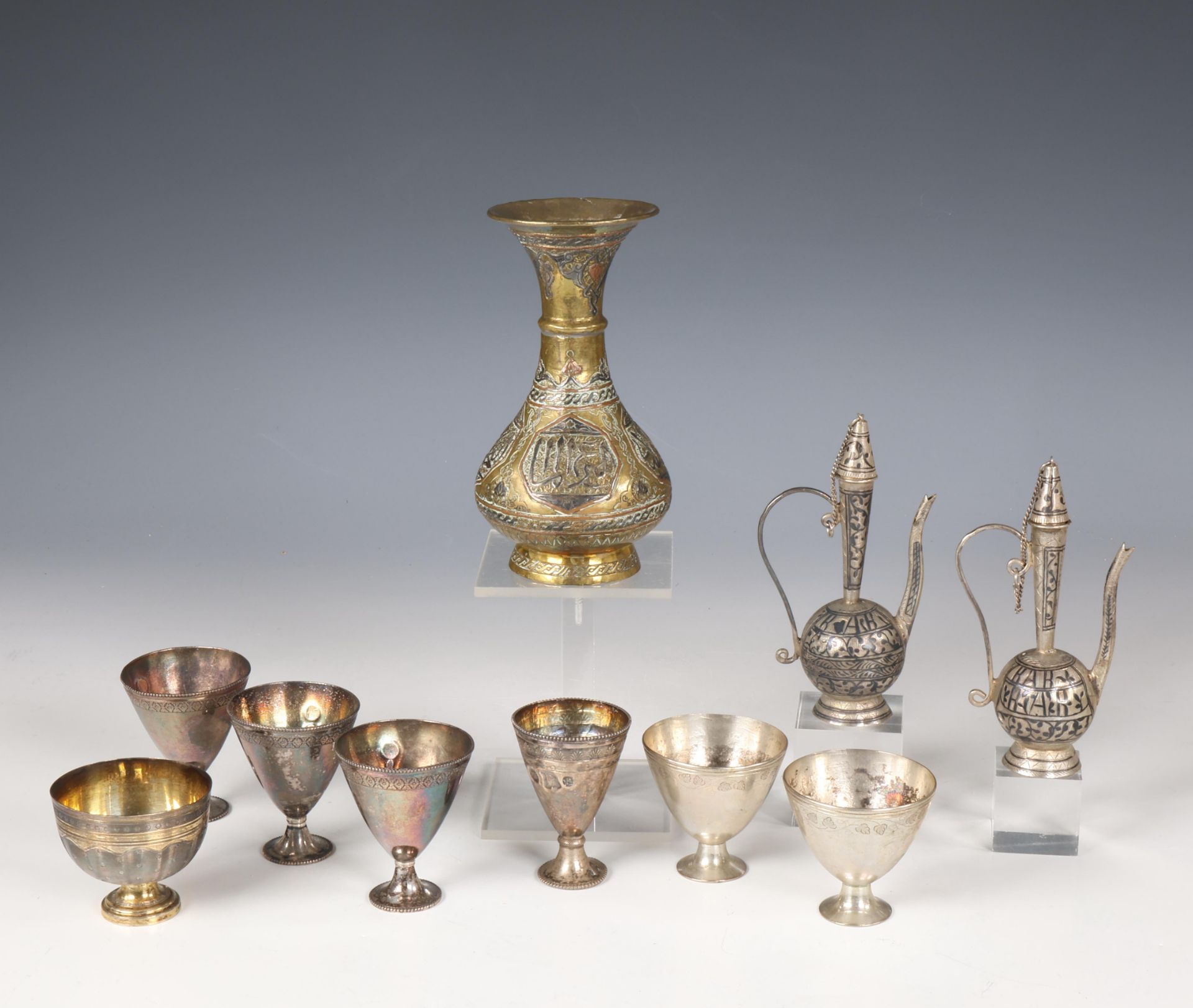 A collection of seven silver alloy cups, two metal niello miniature flasks with lids and a brass vas