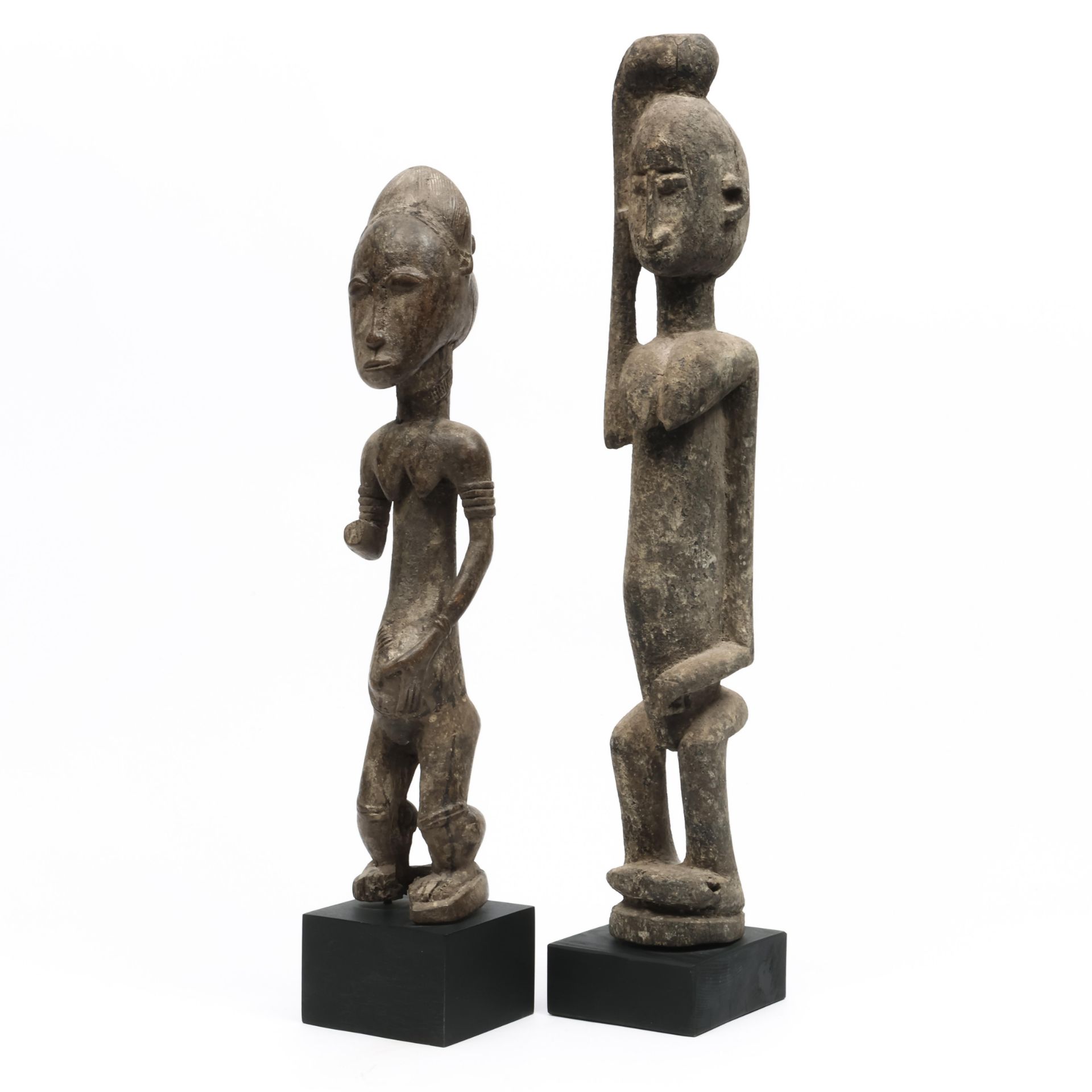 An African standing female figure with one arm missing and a wooden figure with one raised arm.