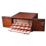 A wooden coin cabinet, 30 x 29 x 17cm, containing 10 trays (4 missing) single-pierced to hou...