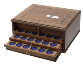 A small wooden cabinet, comprising 6 trays, single pierced to hold 180 Shilling-size coins,...