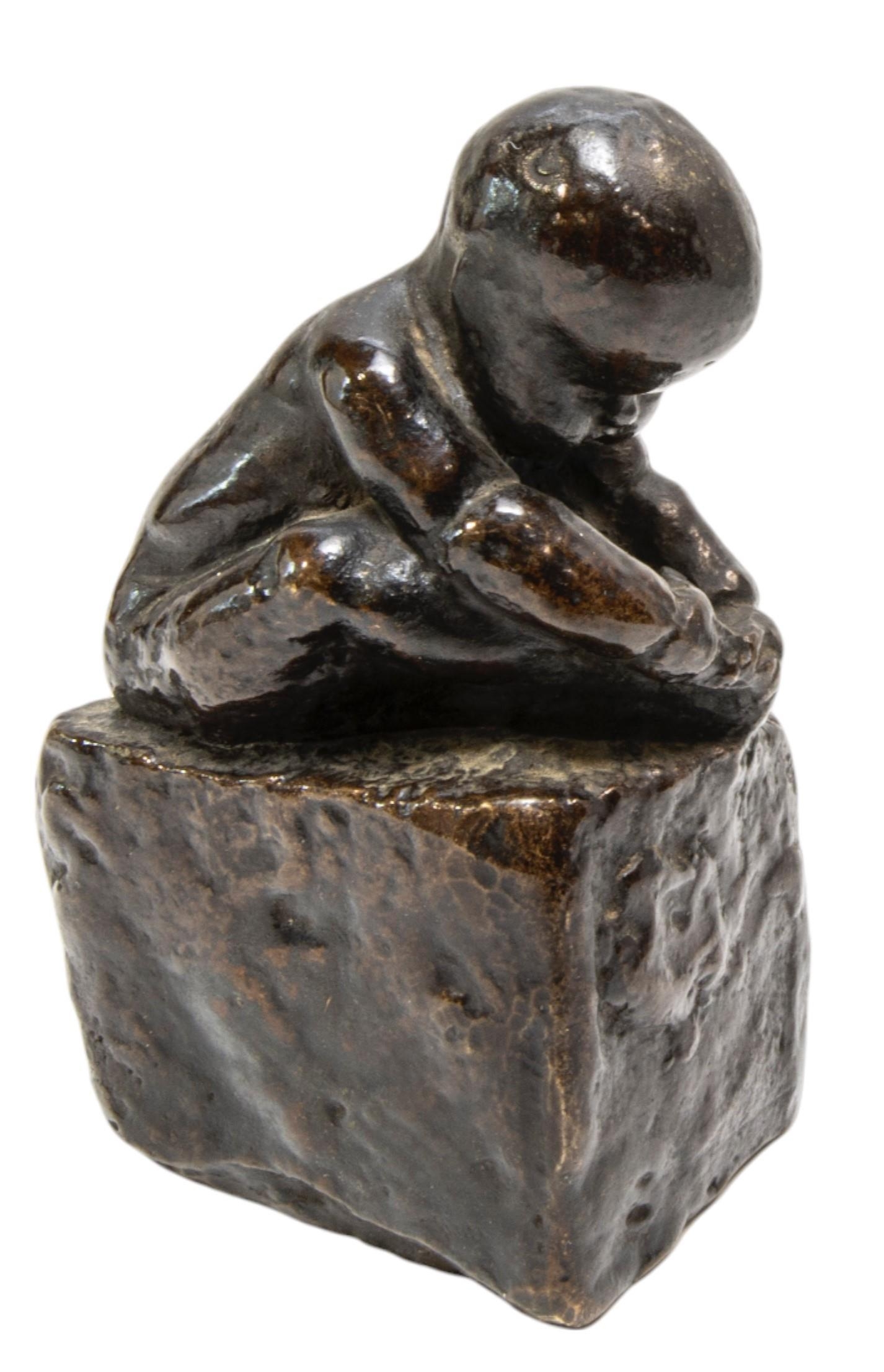 A CAST BRONZE FIGURE OF A CROUCHING INFANT, modelled holding his foot, sat atop a rectangular