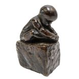 A CAST BRONZE FIGURE OF A CROUCHING INFANT, modelled holding his foot, sat atop a rectangular