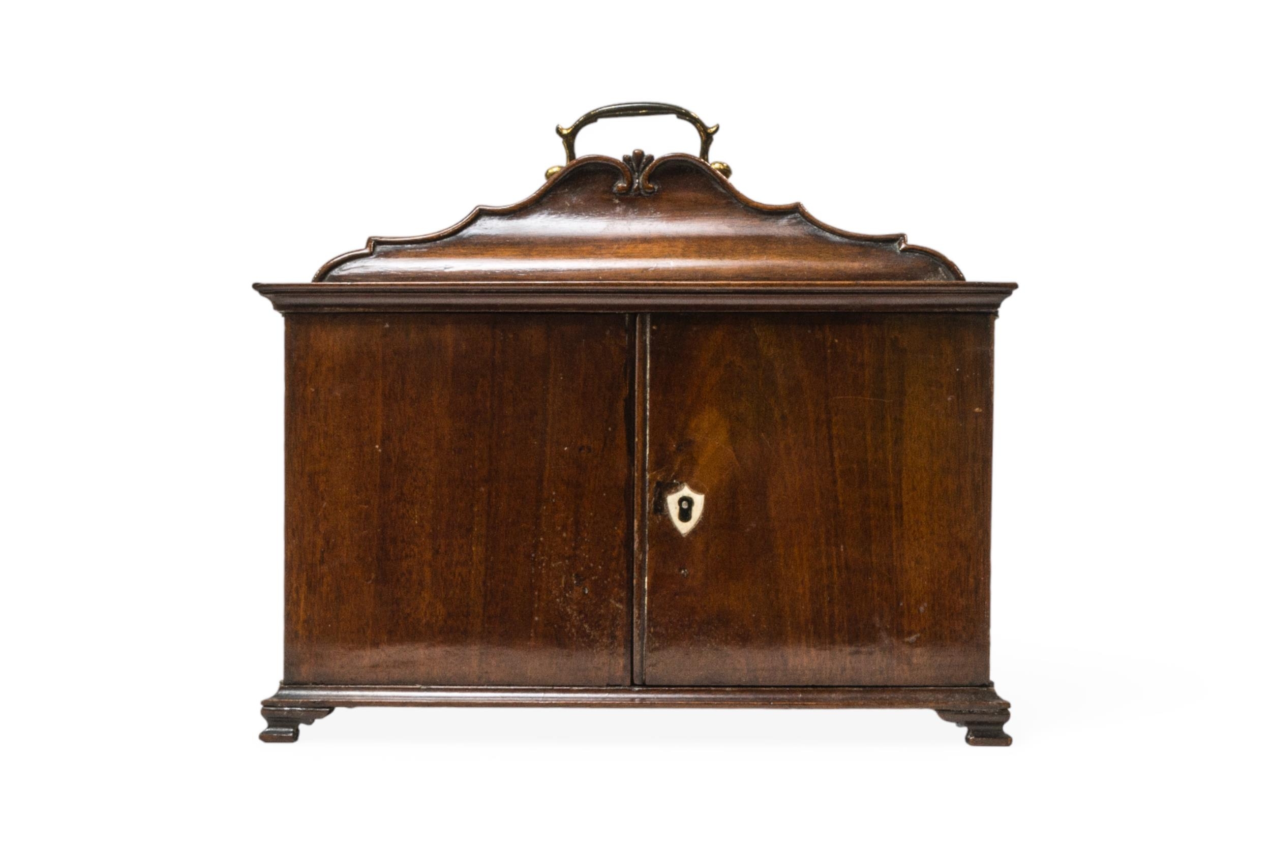 A GEORGE III STYLE MAHOGANY TABLE-TOP 'CABINET', the shaped top with brass swing handle and two