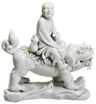 A BLANC-DE-CHINE FIGURE OF A LOHAN 20TH CENTURY modelled as the lohan riding a Buddhist lion,