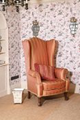 A CARVED WALNUT AND PINK STRIPE UPHOLSTERED WING ARMCHAIR IN 18TH CENTURY STYLE