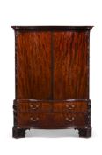 A GEORGE III FIGURED AND CARVED MAHOGANY SERPENTINE CLOTHES PRESS IN THE MANNER OF WILLIAM GOMM