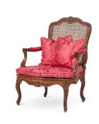 A FRENCH CARVED WALNUT AND BEECH CANED FAUTEUIL IN LOUIS XV STYLE