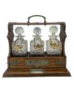 Early 20th century oak three bottle tantalus with originally plated mounts and three cut glass squar