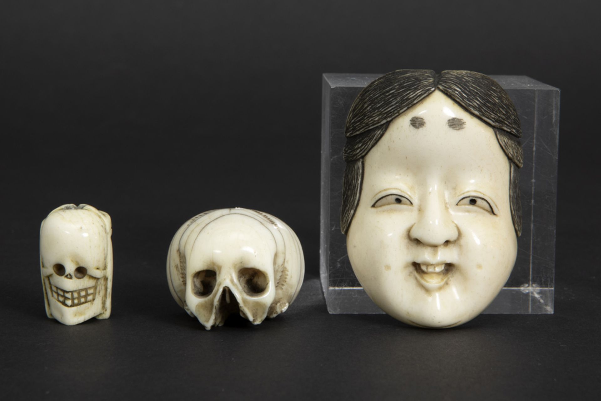 three old smalls in bone : a Japanese mask, a skull and a sculpture with on one side the face of