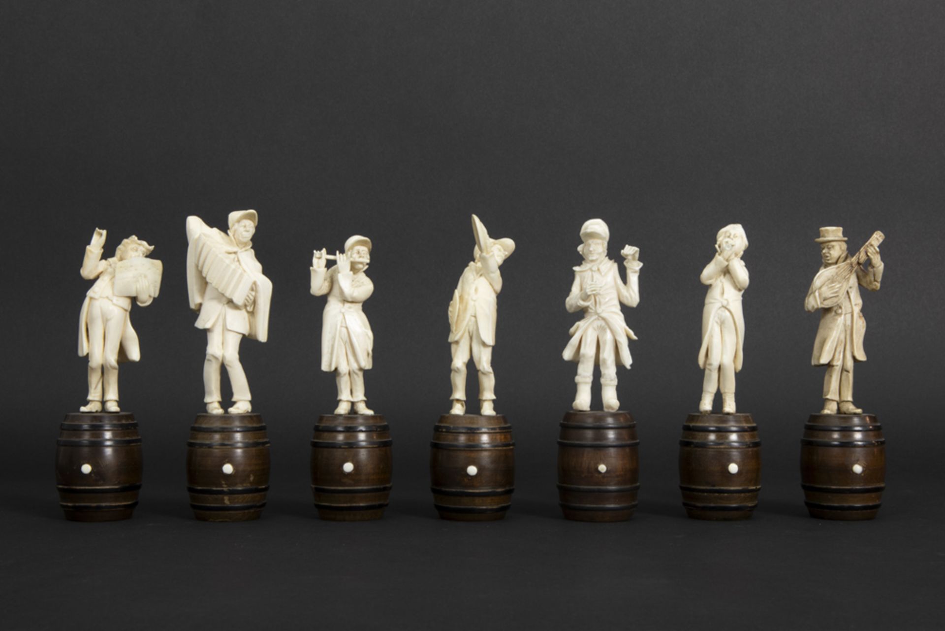 set of seven small antique figures in ivory, each standing on a wooden barrel - depicting a band