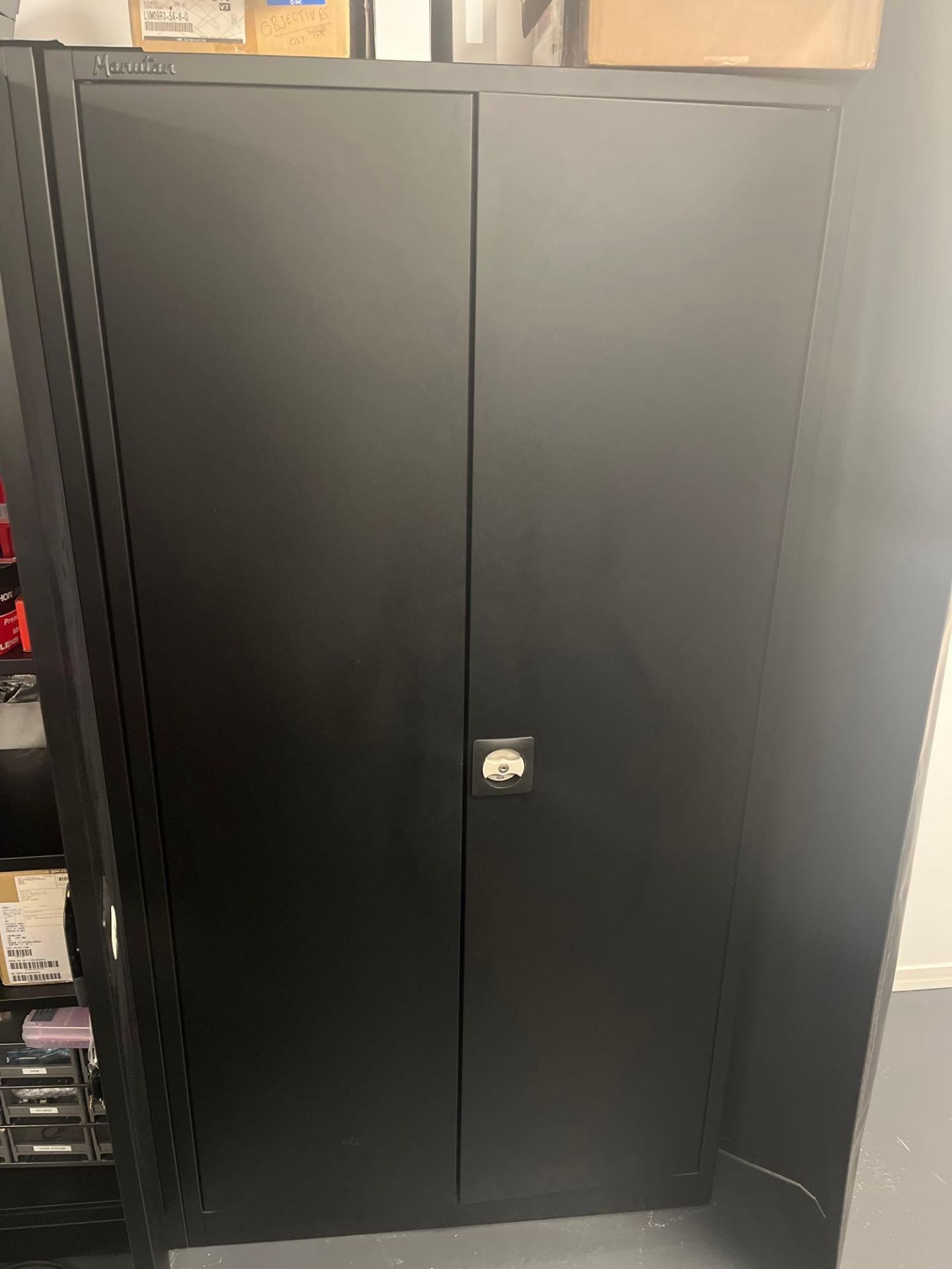 Manutan black metal two door cabinet and contents comprising a quantity of various screws, fixings,