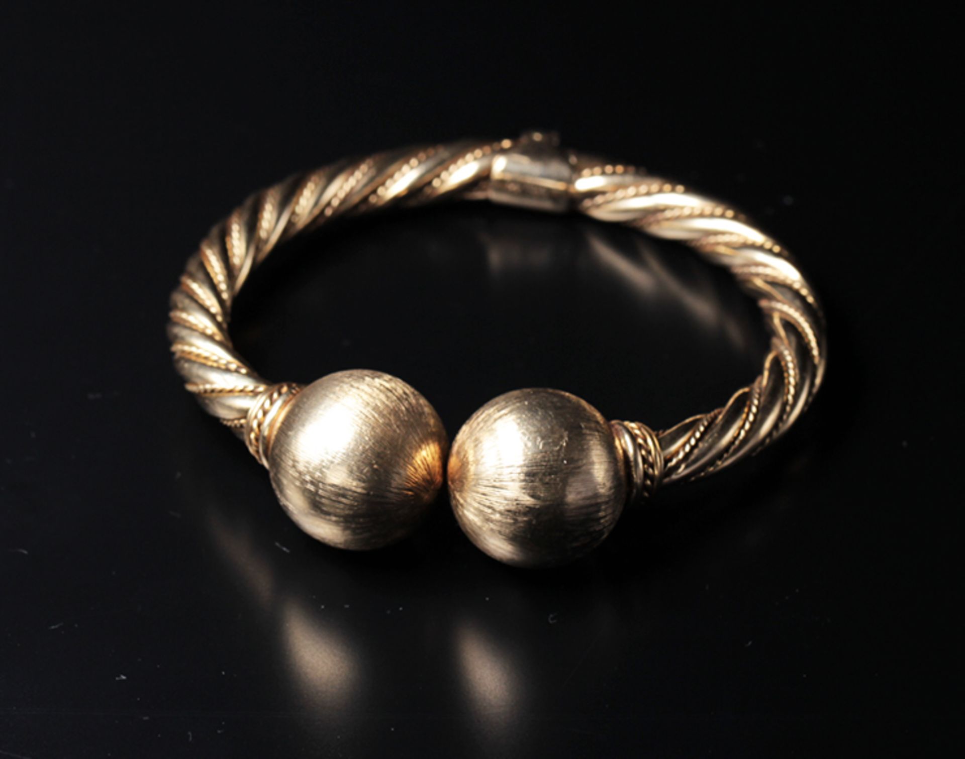 The bangle is made of twisted gold wires and has round spheres at the end.The spheres have a