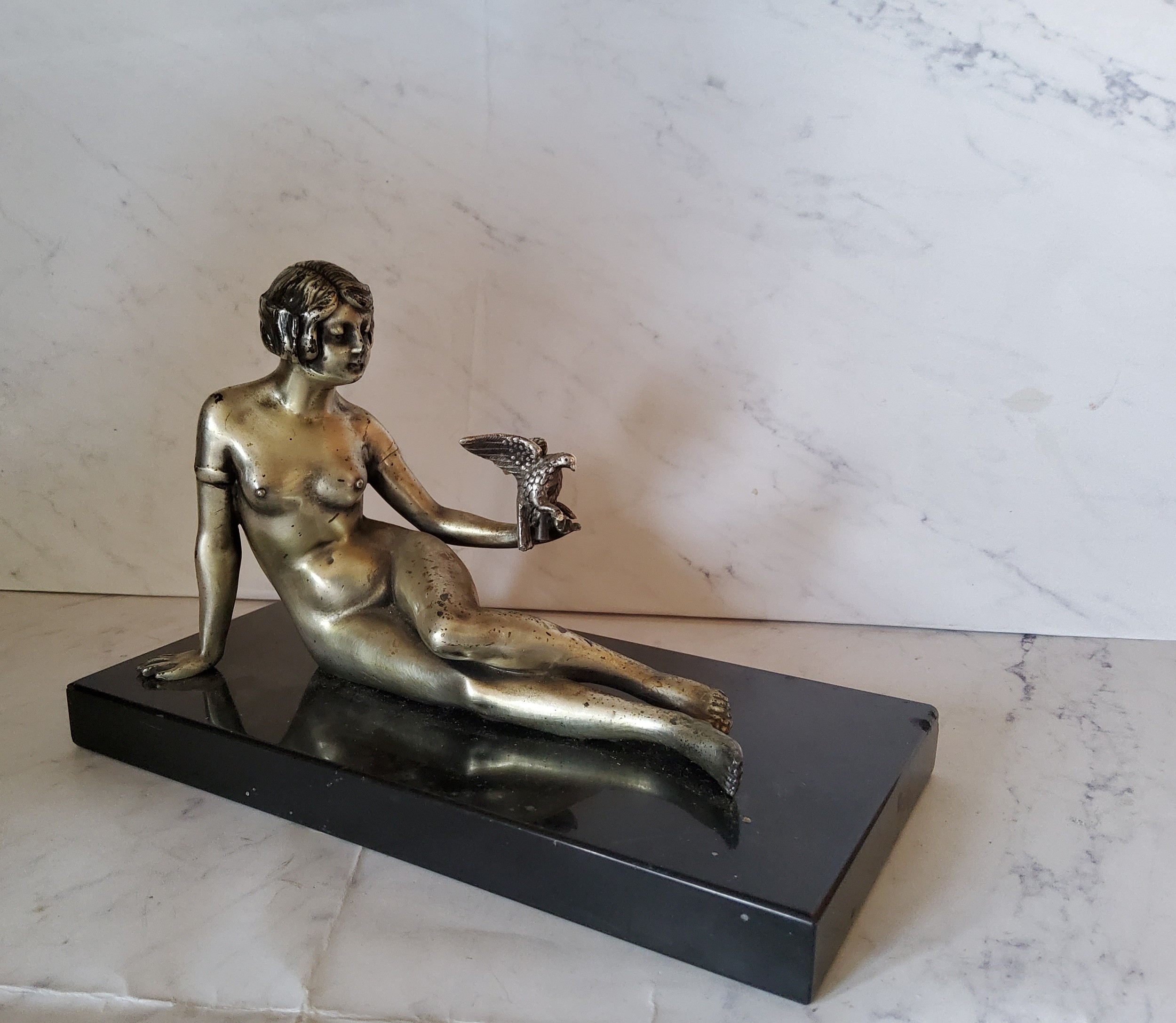 Art Deco, a silvered bronze, a lady with a bird, reclining, black rectangular marble base, 22cm wide